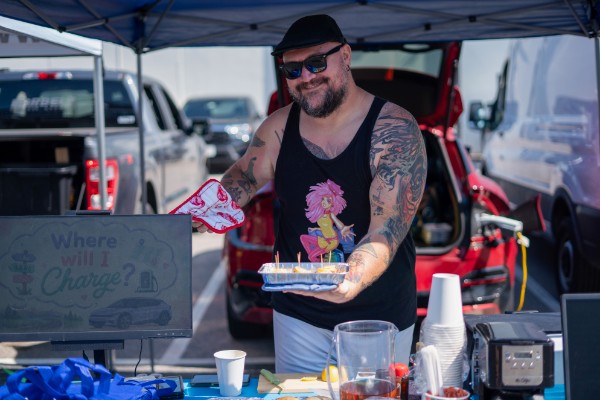 Man standing at a booth at the Glizzies n' Gainz event, holding out food that was made with help from his electric vehicle.